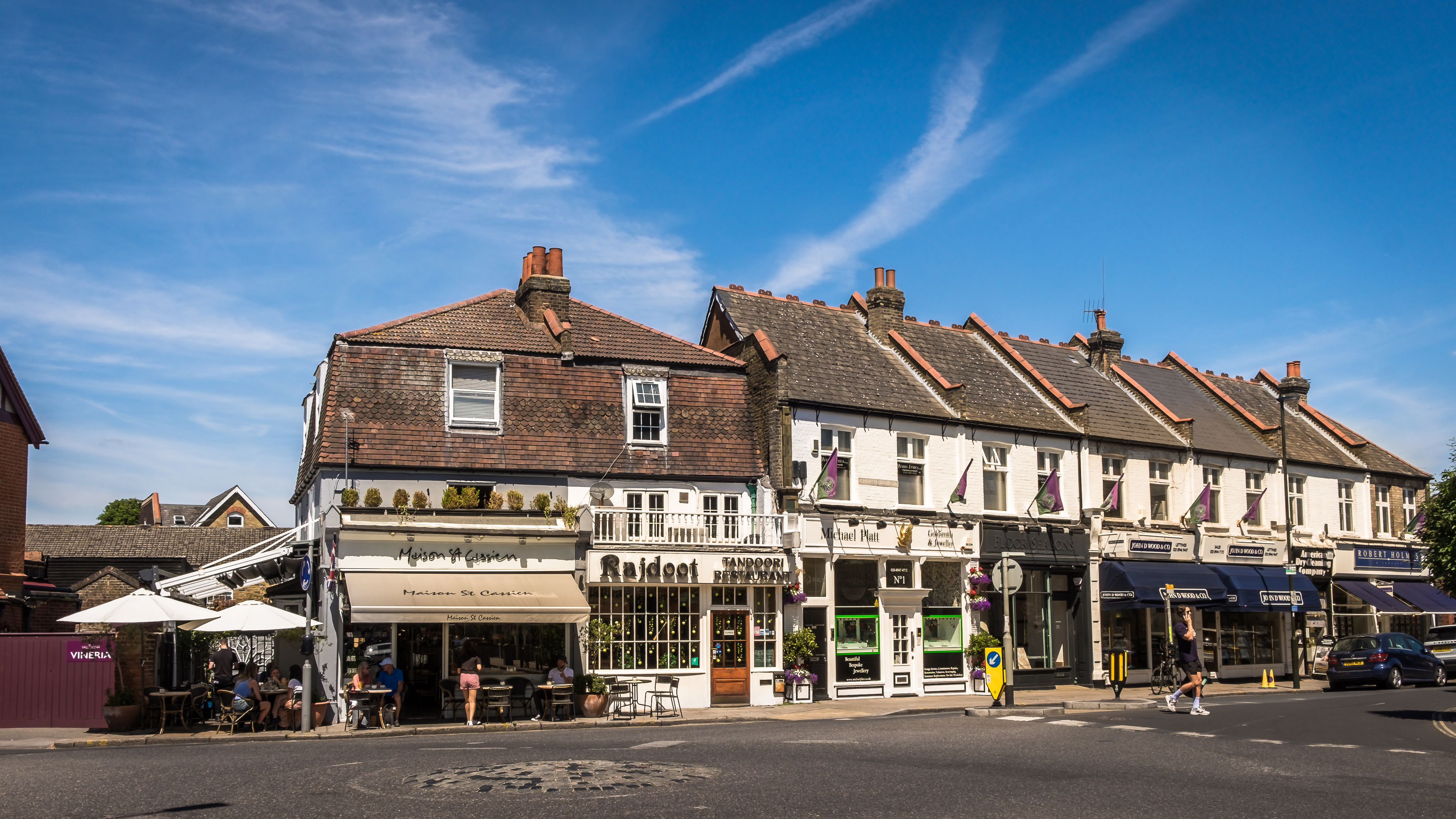 A row of shops and caf&eacute;s in Wimbledon Village on a sunny day, including Maison St Cassien and other local businesses.